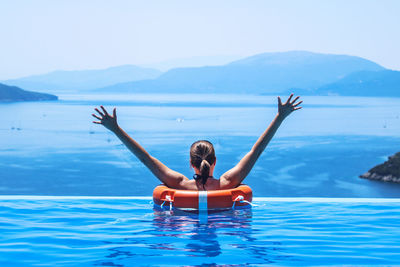 Rear view of happy woman in infinity pool by sea against clear sky