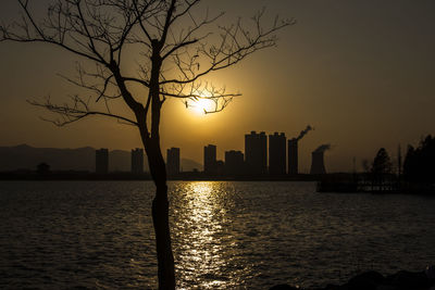 Silhouette of city at waterfront during sunset