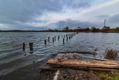 Wooden posts in lake against sky