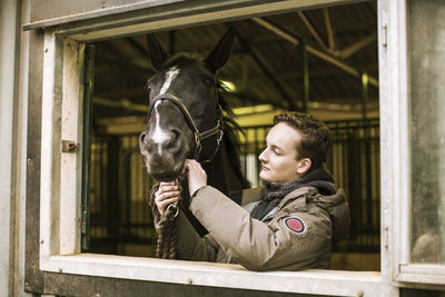 Young man with horse in stable