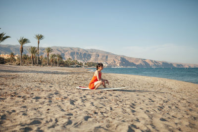 Full length of man sitting on sand at beach against sky