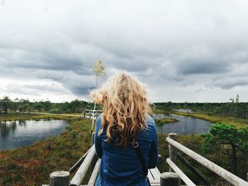 Rear view of woman standing by lake against sky