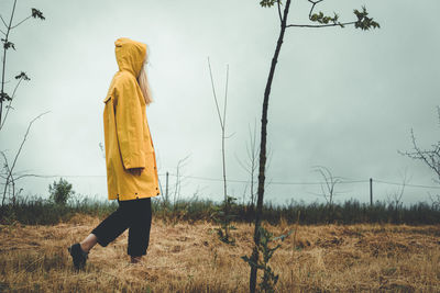 Girl in a yellow raincoat on a cloudy rainy walks between the trees. concept of loneliness