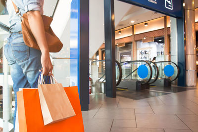 Midsection of woman with shopping bags standing in shopping mall