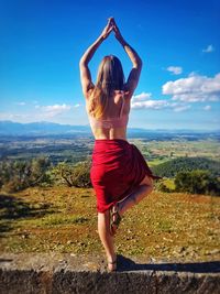 Rear view of woman practicing yoga against sky