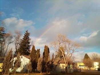 Scenic view of rainbow over trees and buildings against sky