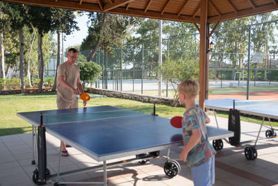 Eight year old blond boy plays ping pong with his father on a special table tennis court, fun summer