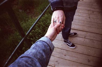 Cropped image of woman holding man hand on footbridge