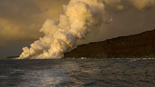 Scenic view of sea and lava steam against sky