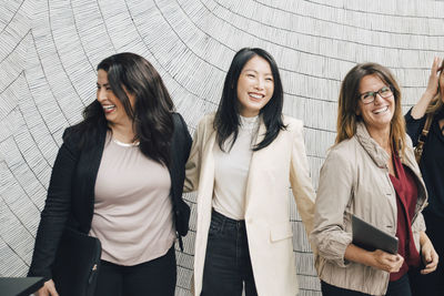 Smiling multi-ethnic female business professionals standing against wall at office