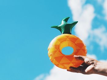 Cropped hand of person holding inflatable pineapple against sky