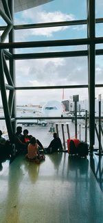 People waiting at airport against sky seen through window