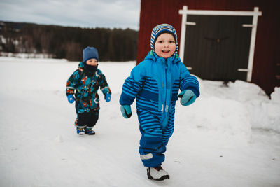 Young twin boys smiling walking in snow in scandinavian farm by barn