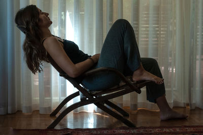 Side view of woman sitting on chair at home