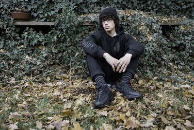 Portrait of young man sitting against creeper plants in yard