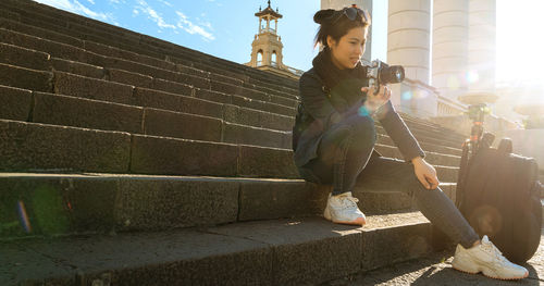 Woman sitting on steps with camera during day