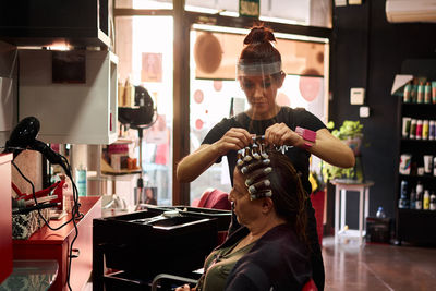 Hairdresser combs a client with a face shield in her salon