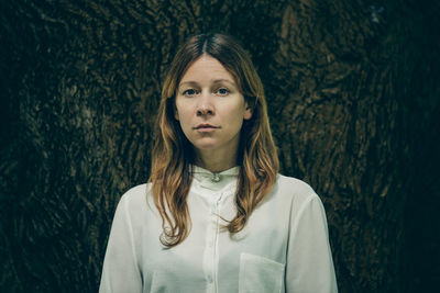 Portrait of mid adult woman standing against tree trunk in forest