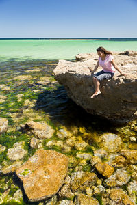 Woman sitting on rock by sea against sky