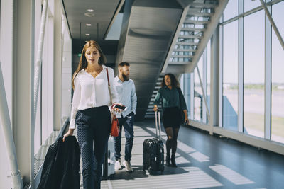 Young businesswoman walking in front of colleagues in corridor at airport