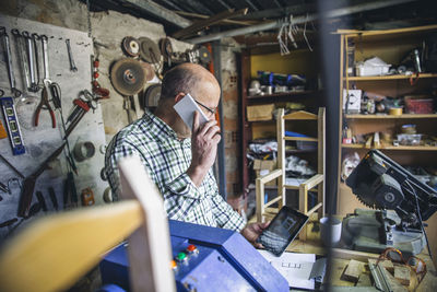 Senior man talking on phone while standing at workshop
