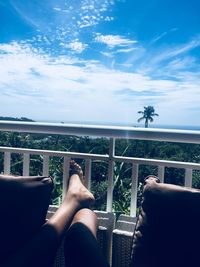 Low section of woman sitting by plants against sky