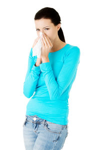 Young woman sneezing while standing over white background