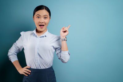 Portrait of smiling young woman standing against blue background