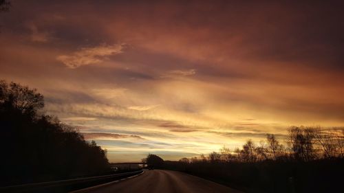 Road by silhouette trees against sky at sunset