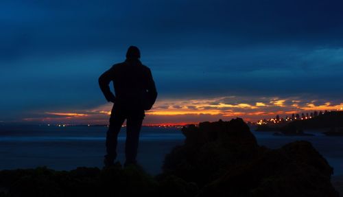 Rear view of silhouette mature man standing by sea against cloudy sky during sunset