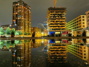 Illuminated buildings by river against sky in city at night