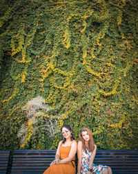 Portrait of female friends sitting on bench against plants