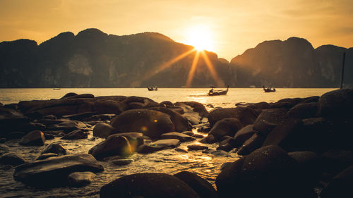 Rocks on beach against sky during sunset