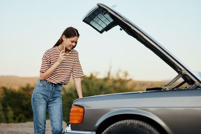 Side view of woman standing against car