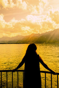 Rear view of woman looking at lake against sky