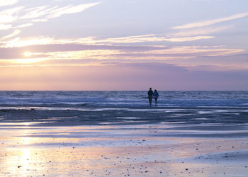 Couple walking at beach against sky during sunset