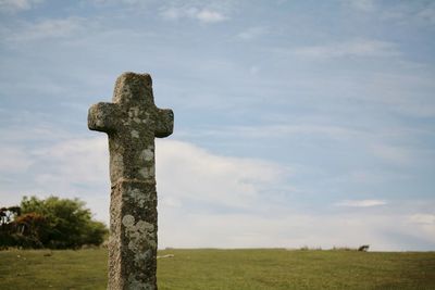 Stone cross on field against sky