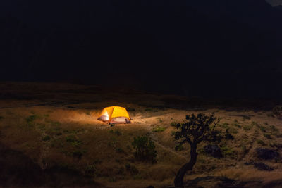 Illuminated lighting equipment on rock against sky at night