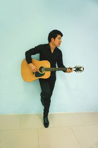 Full length of man playing guitar against wall