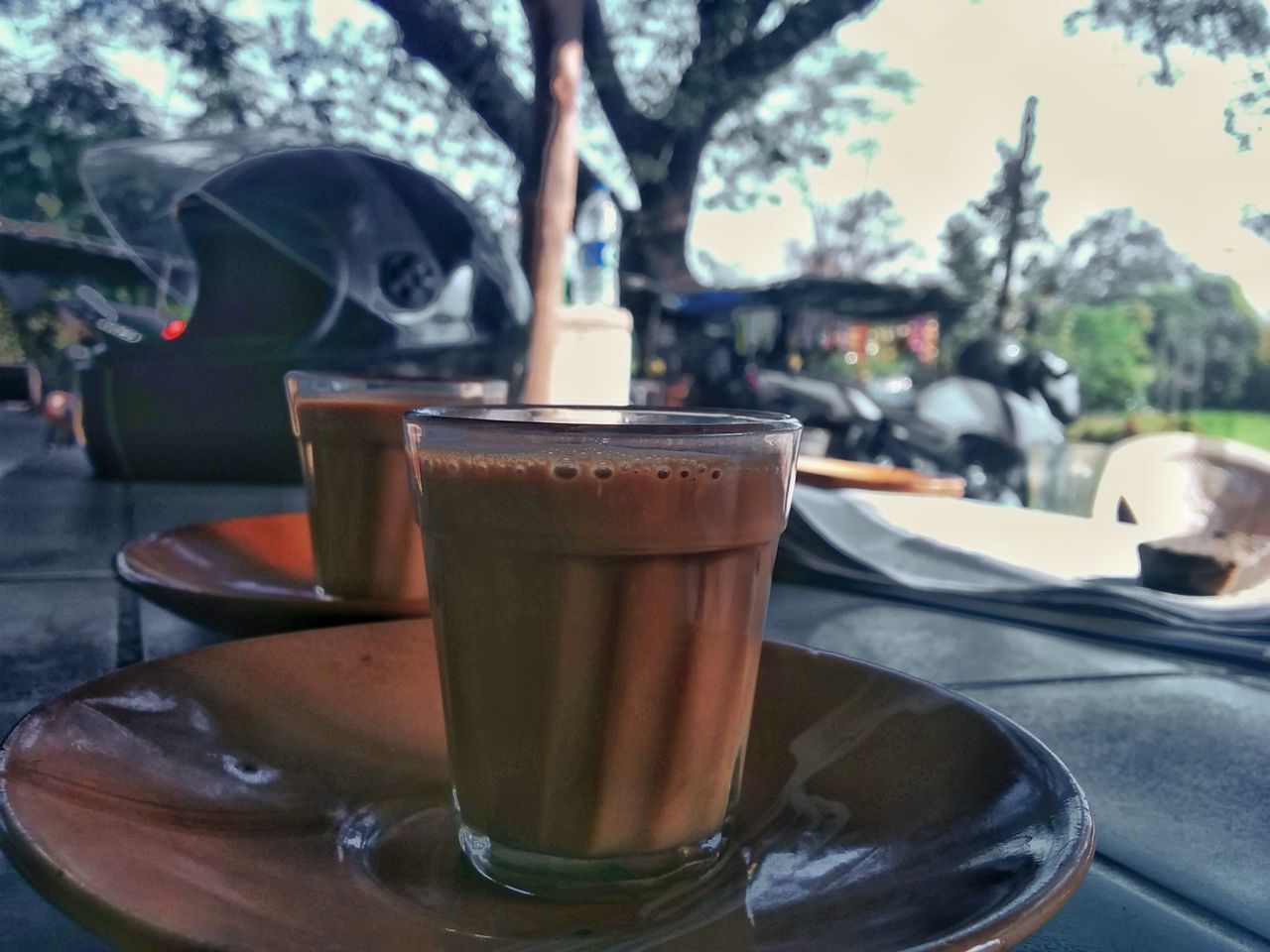 CLOSE-UP OF COFFEE CUP ON TABLE AGAINST TREES