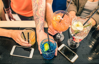 Cropped hands of friends holding drinks on counter in bar