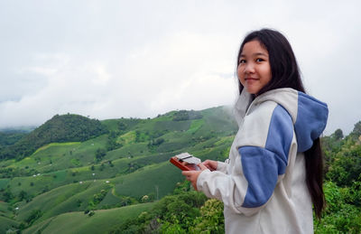 Little girl play a kalimba or mbira at the hillside with agriculture field  against sky