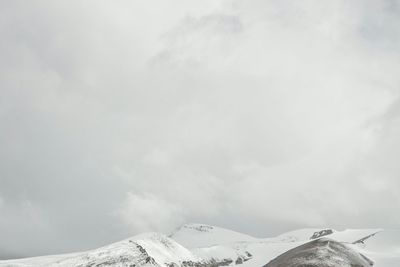 Low angle view of snow covered mountain against cloudy sky