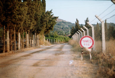 Road sign on street amidst fence