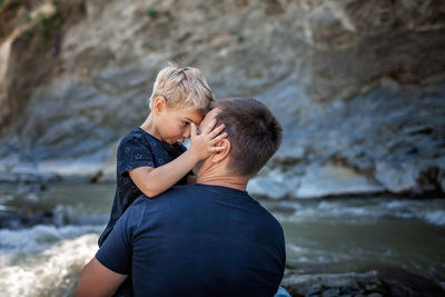 Like father like son. middle aged father embracing cute little son on the bank of river, family 