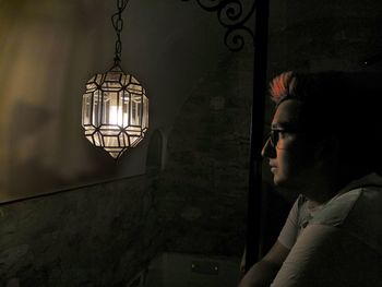 Close-up of young man looking at illuminated lighting equipment against wall