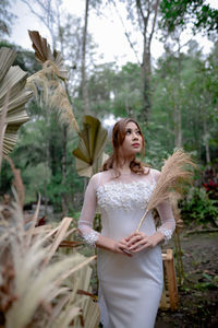 Portrait of young woman standing against trees