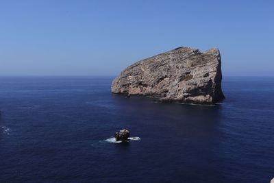 Rock formation in sea against clear blue sky