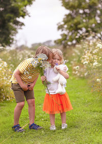 Low angle view of boy and girl standing on grass with flowers