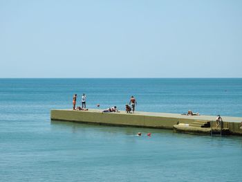 People on pier over sea against clear sky